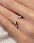 Close-up of a hand wearing an open diamond enhancer ring on a neutral background