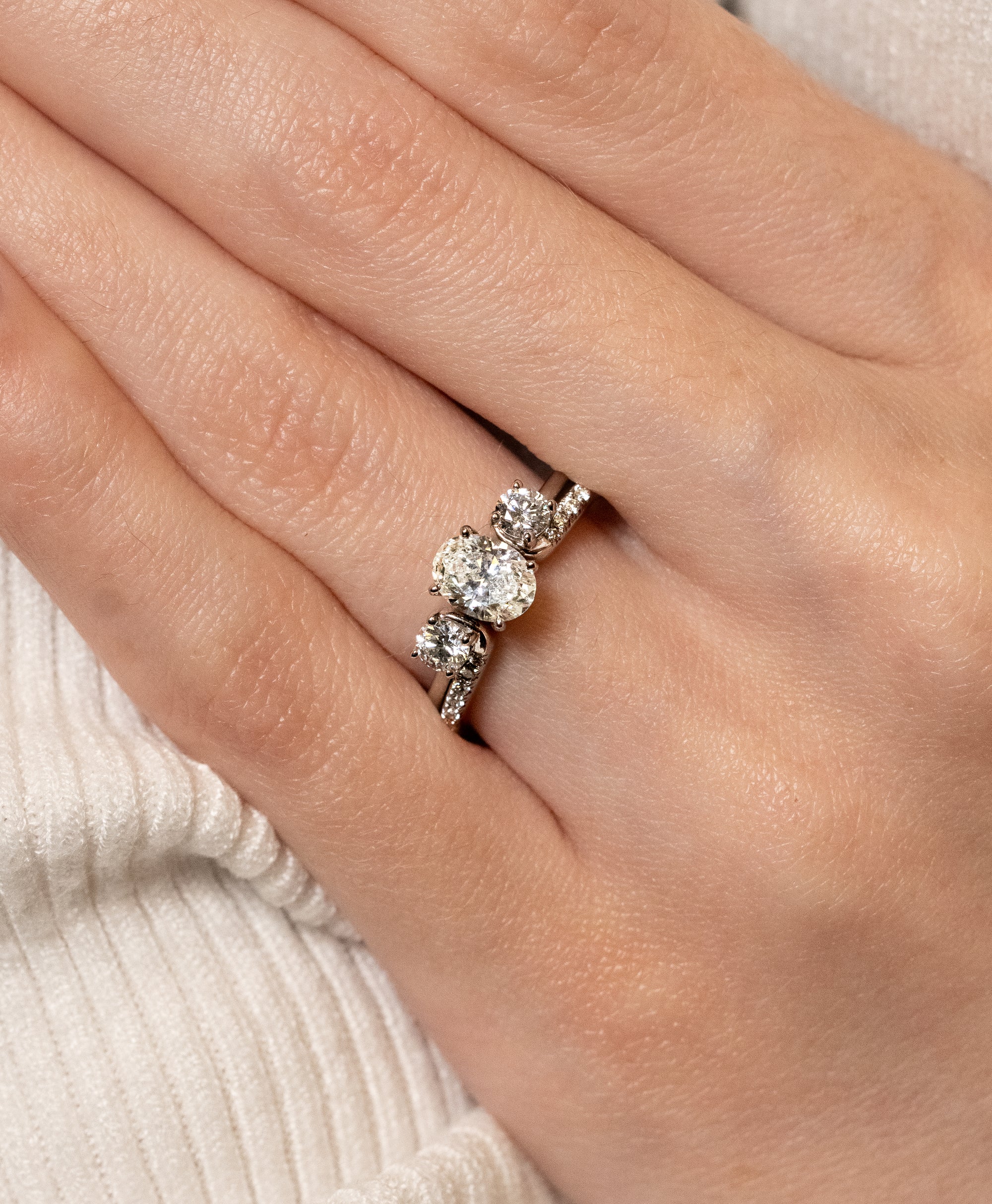 Diamond enhancer  ring  with oval diamond solitaire on a person's finger with a neutral background