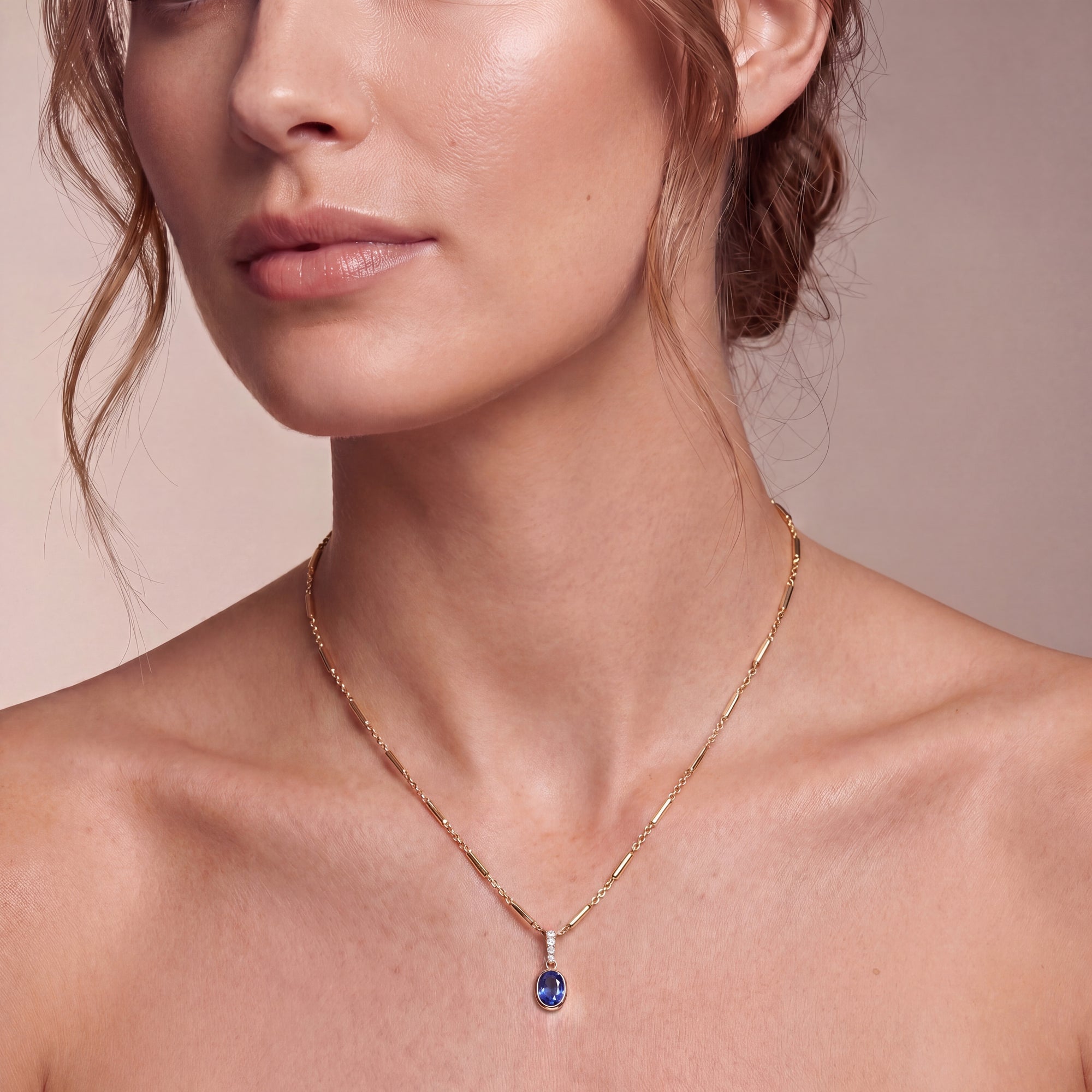 person with curled hair wearing a gold necklace with a bar chain and a blue oval pendant on a neutral background