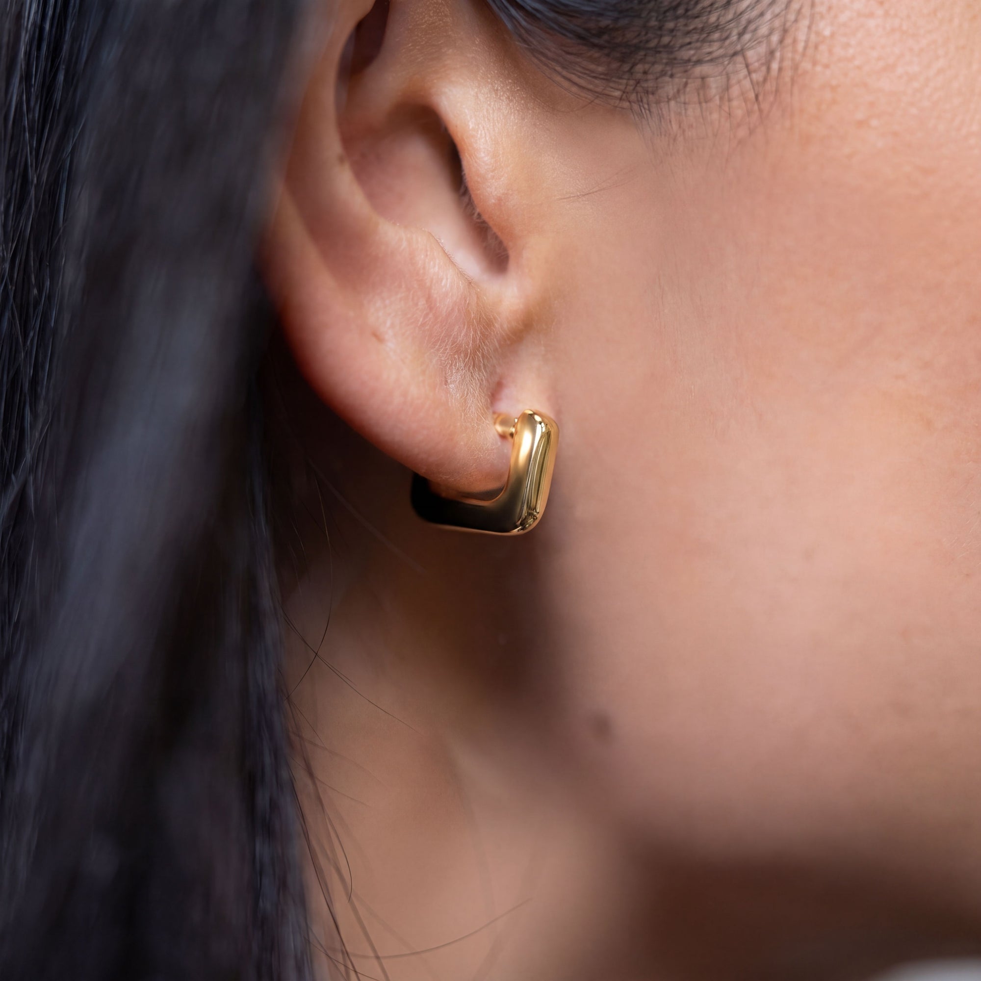 close up of a person wearing a gold square hoop earring