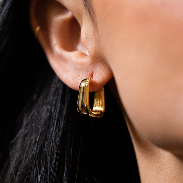 Gold hoop earrings worn by a person with dark hair.