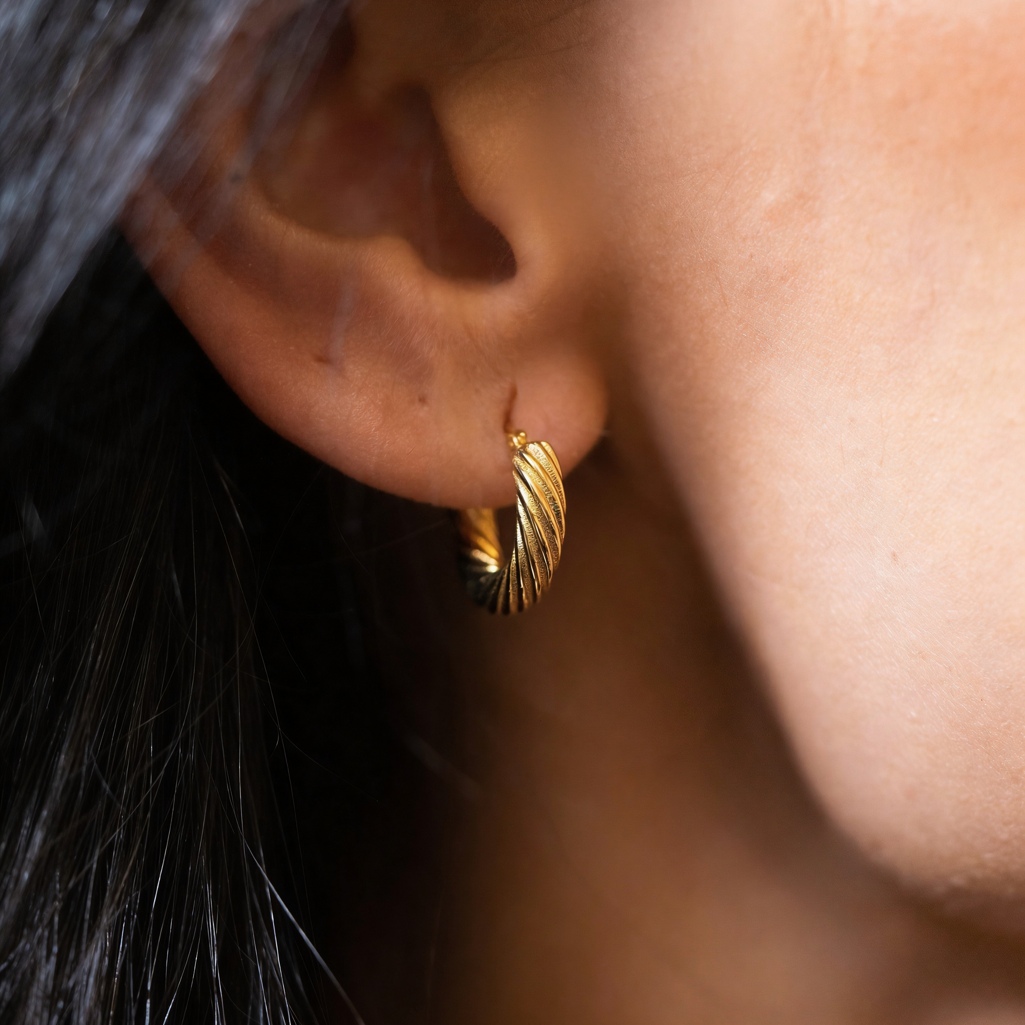 close up of an ear with a gold hoop with a twisted design 