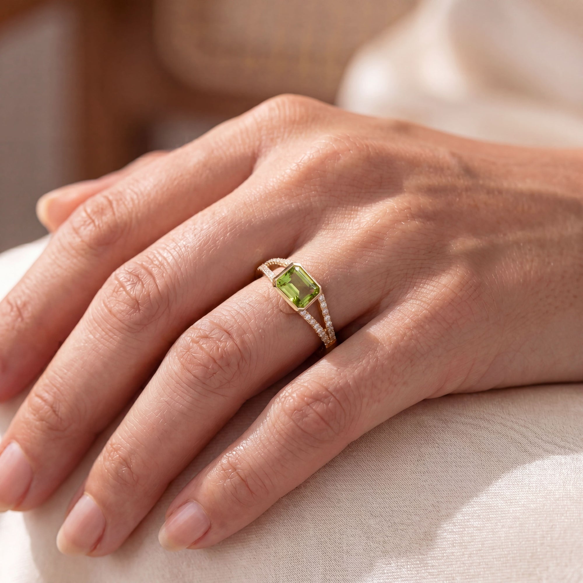 close up of a hand wearing a yellow ring with a green center and diamonds on a neutral background
