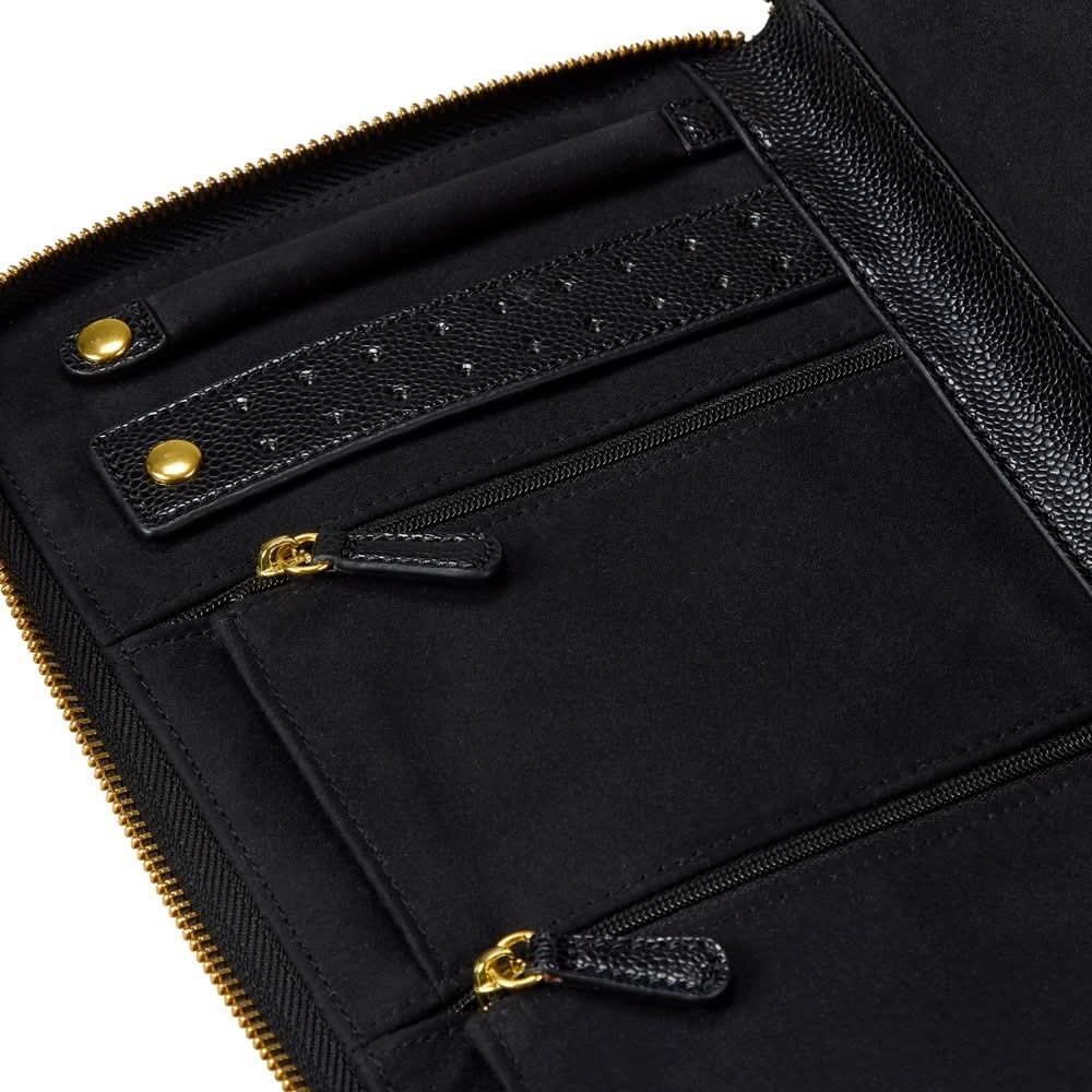 Close-up of a black leather and fabric zip-around jewelry organizer with gold-tone hardware, showing interior compartments, a textured strap, and zipper pulls on a white background.