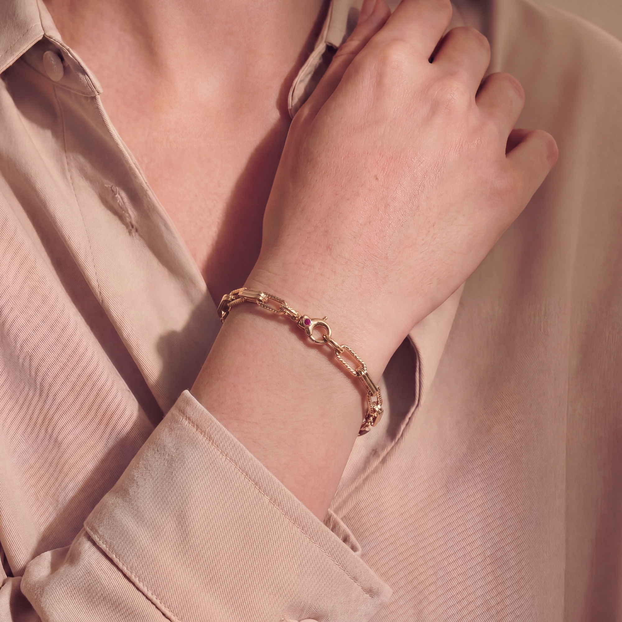 Close-up of a hand wearing a gold bracelet with a pink shirt.