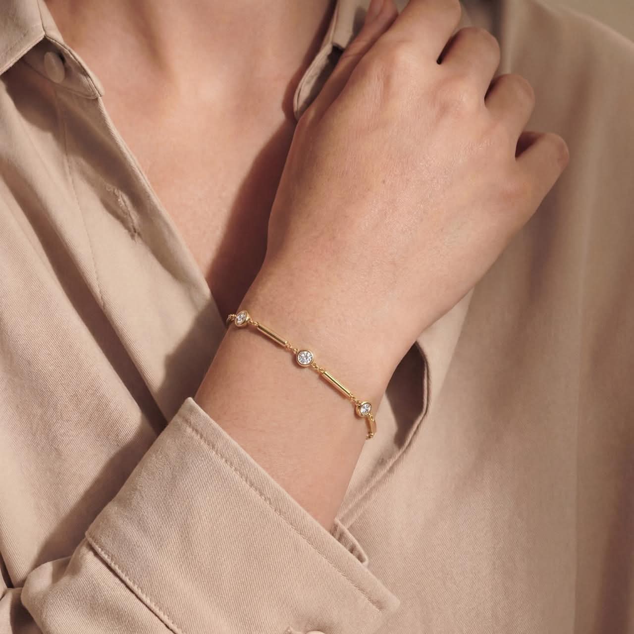 Gold bracelet with small diamonds on a wrist, wearing a beige shirt.