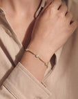 Gold bracelet with small diamonds on a wrist, wearing a beige shirt.