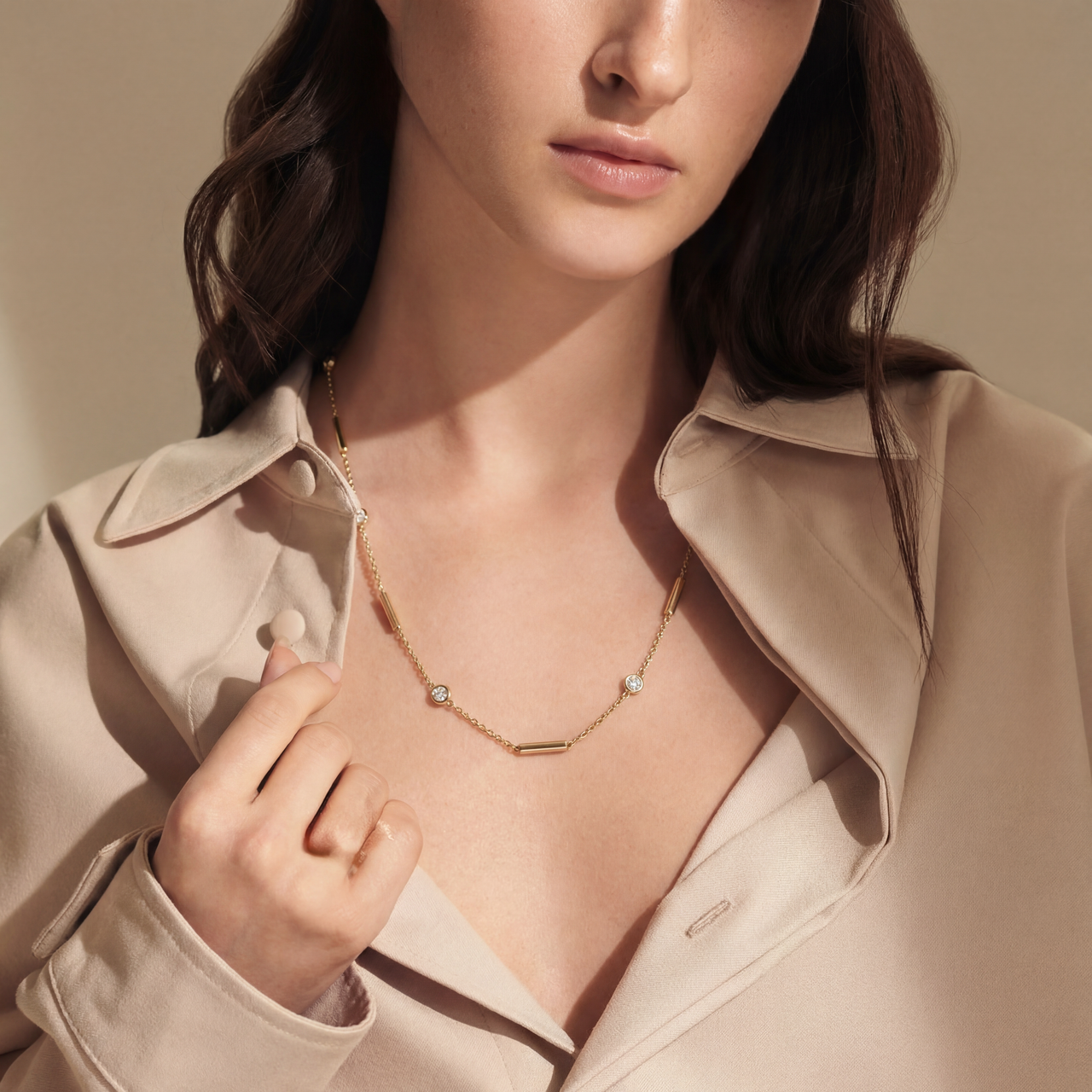 Woman wearing a gold necklace with a beige jacket against a neutral background