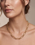 Close-up of a person wearing a gold chain necklace against a neutral background