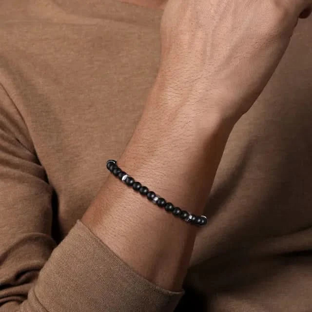 Black beaded bracelet on a wrist with a brown background