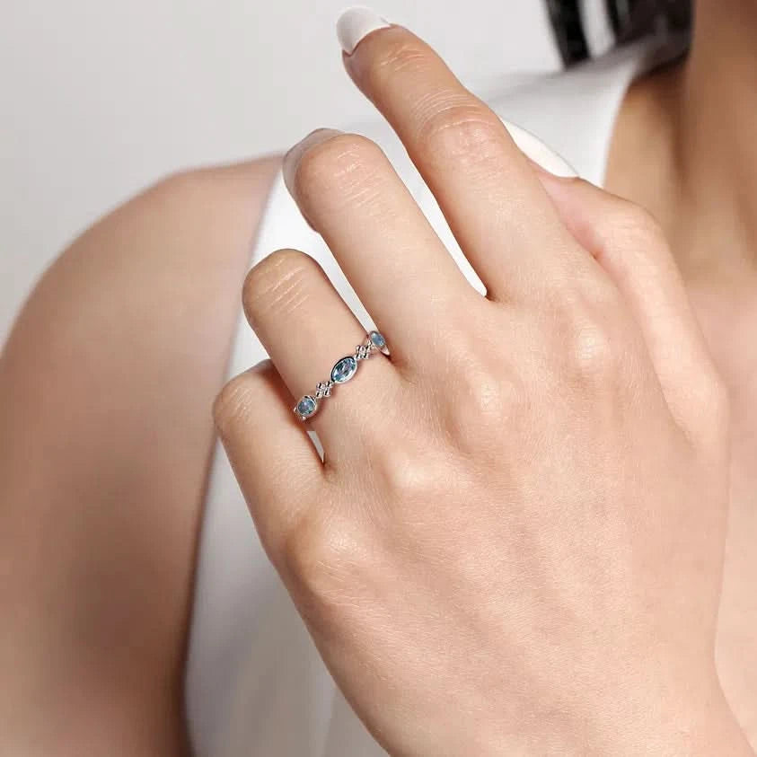 Close-up of a hand wearing a blue stone ring on a neutral background