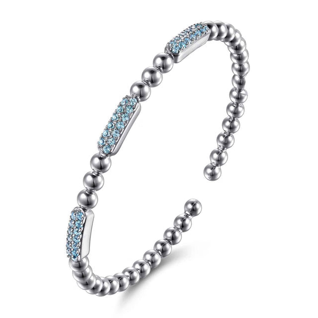 A silver-toned beaded cuff bracelet with three rectangular inlays set with light blue topaz shown angled on a clean white background.