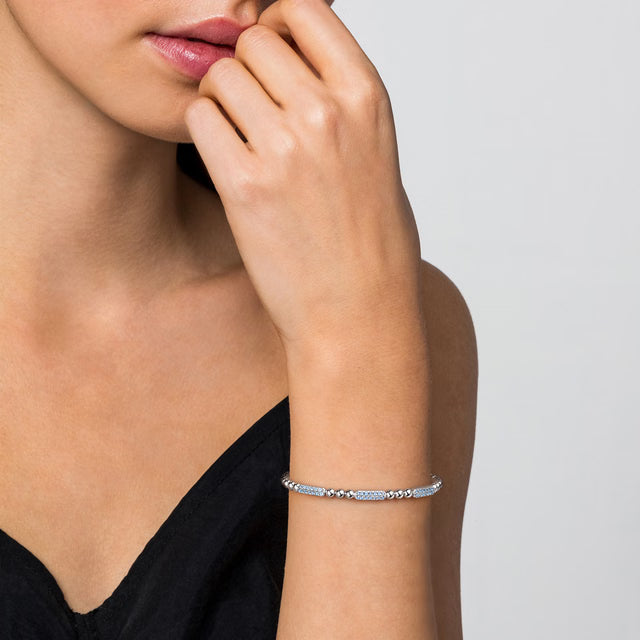 Woman wearing a silver bracelet with blue topaz stones on a neutral background