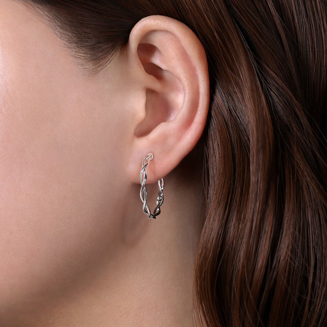 Close-up of an ear wearing a delicate twisted silver earring with a blurred background