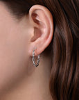Close-up of an ear wearing a delicate twisted silver earring with a blurred background
