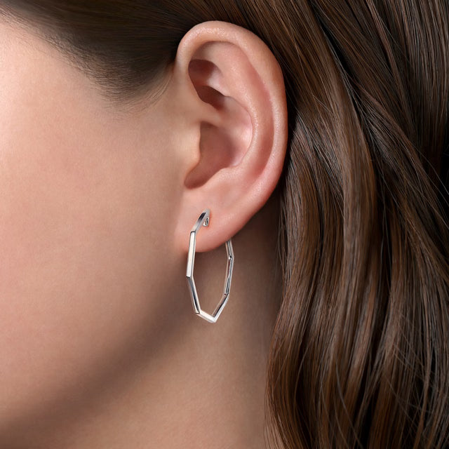 silver geometric hoop earrings worn by a person with brown hair.