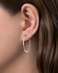 silver geometric hoop earrings worn by a person with brown hair.