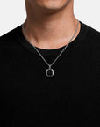 Person wearing a silver necklace with a hexagonal pendant on a plain background