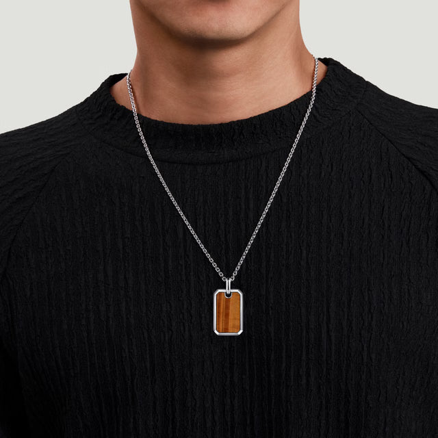 Person wearing a necklace with a rectangular pendant on a plain background
