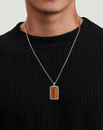 Person wearing a necklace with a rectangular pendant on a plain background