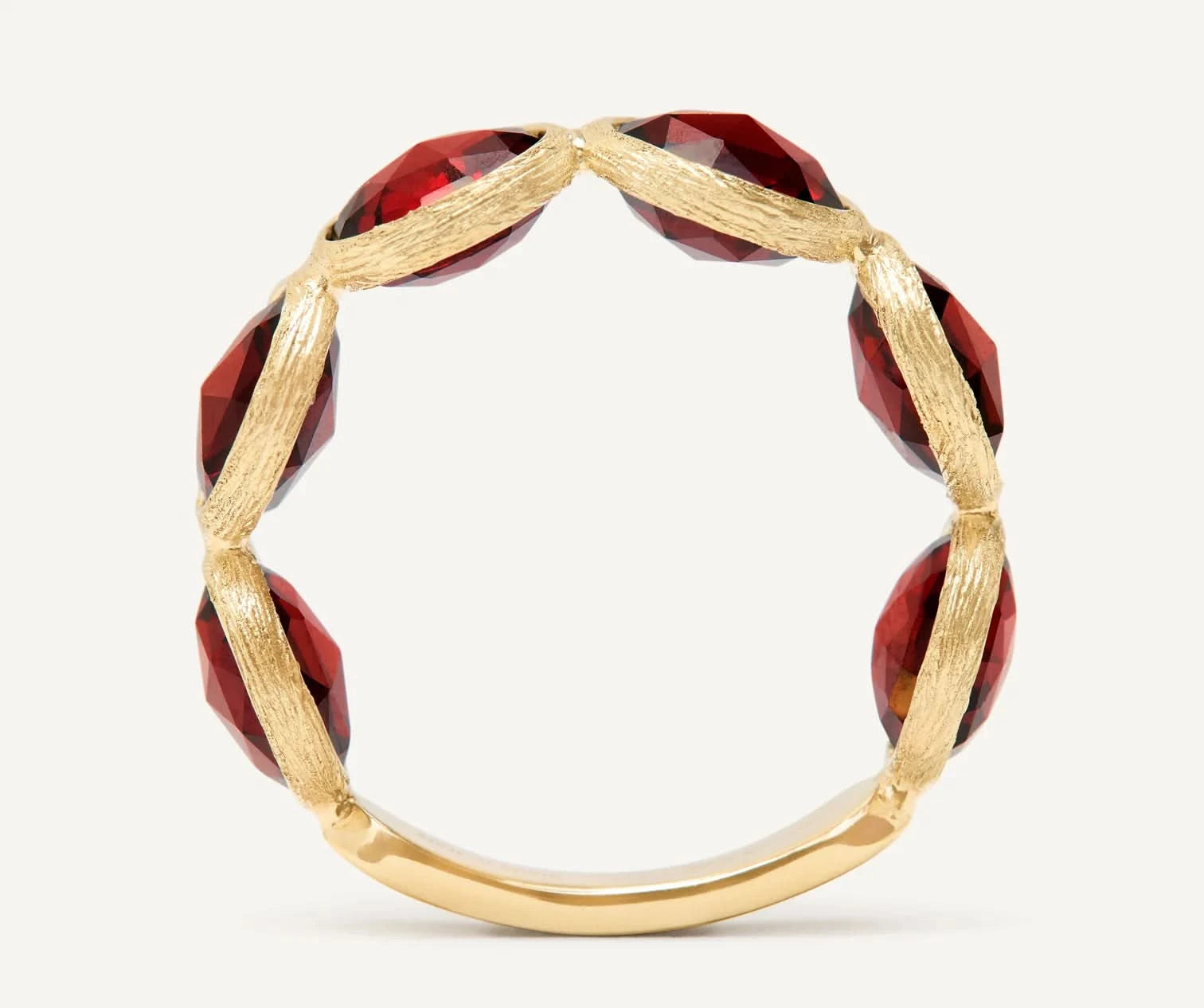 A gold ring featuring faceted deep red gemstone segments set along the band, photographed against a clean off-white background.