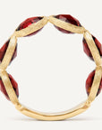 A gold ring featuring faceted deep red gemstone segments set along the band, photographed against a clean off-white background.