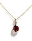 A gold necklace with a teardrop-shaped dark red gemstone pendant, shown on a clean white background with a soft shadow.