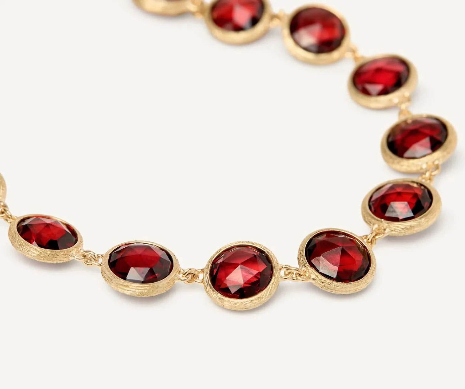 A close-up of a gold chain bracelet featuring round rose-cut,  deep red gemstones in gold bezel settings, set against a clean white background.