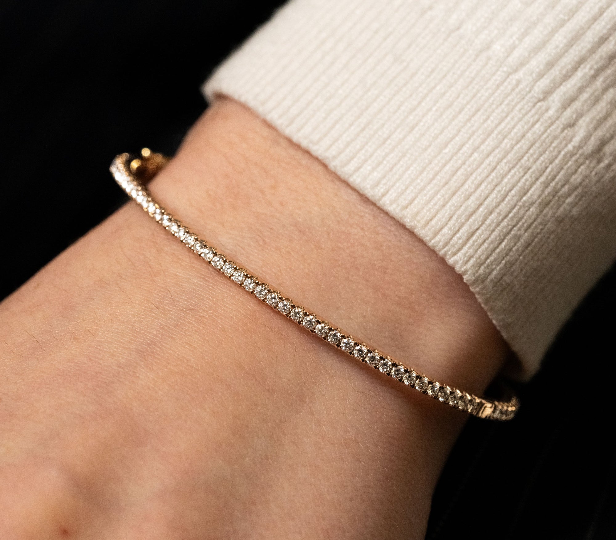 Gold bracelet with diamonds on a wrist against a black background