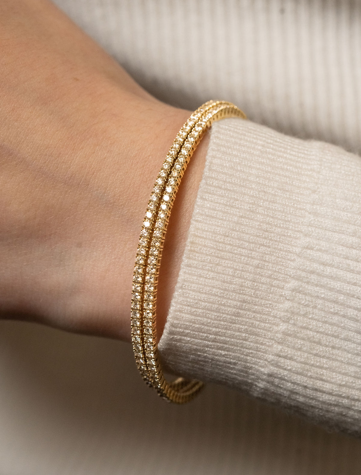 yellow gold double flexible tennis bracelet on a wrist with a beige sweater background