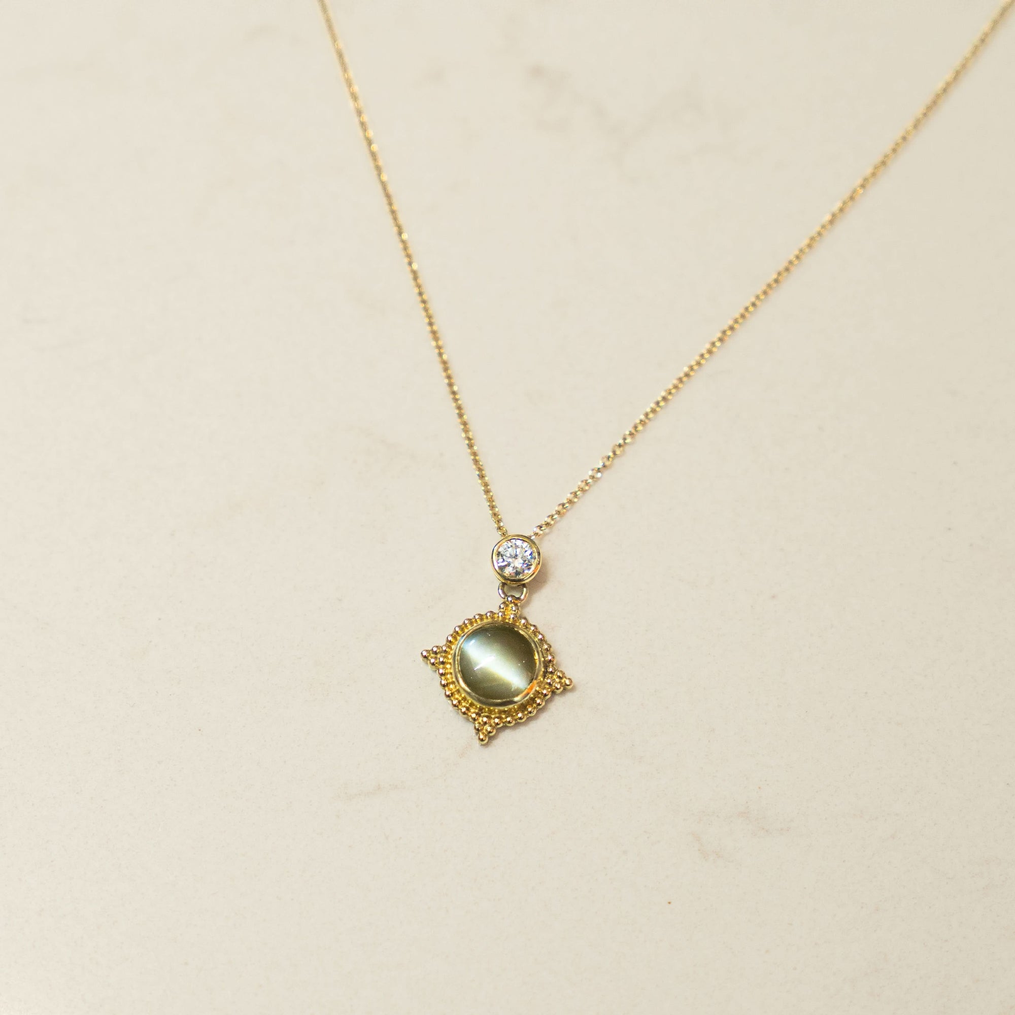 Gold necklace with a diamond and green stone pendant on a beige background