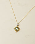 Gold necklace with a diamond and green stone pendant on a beige background