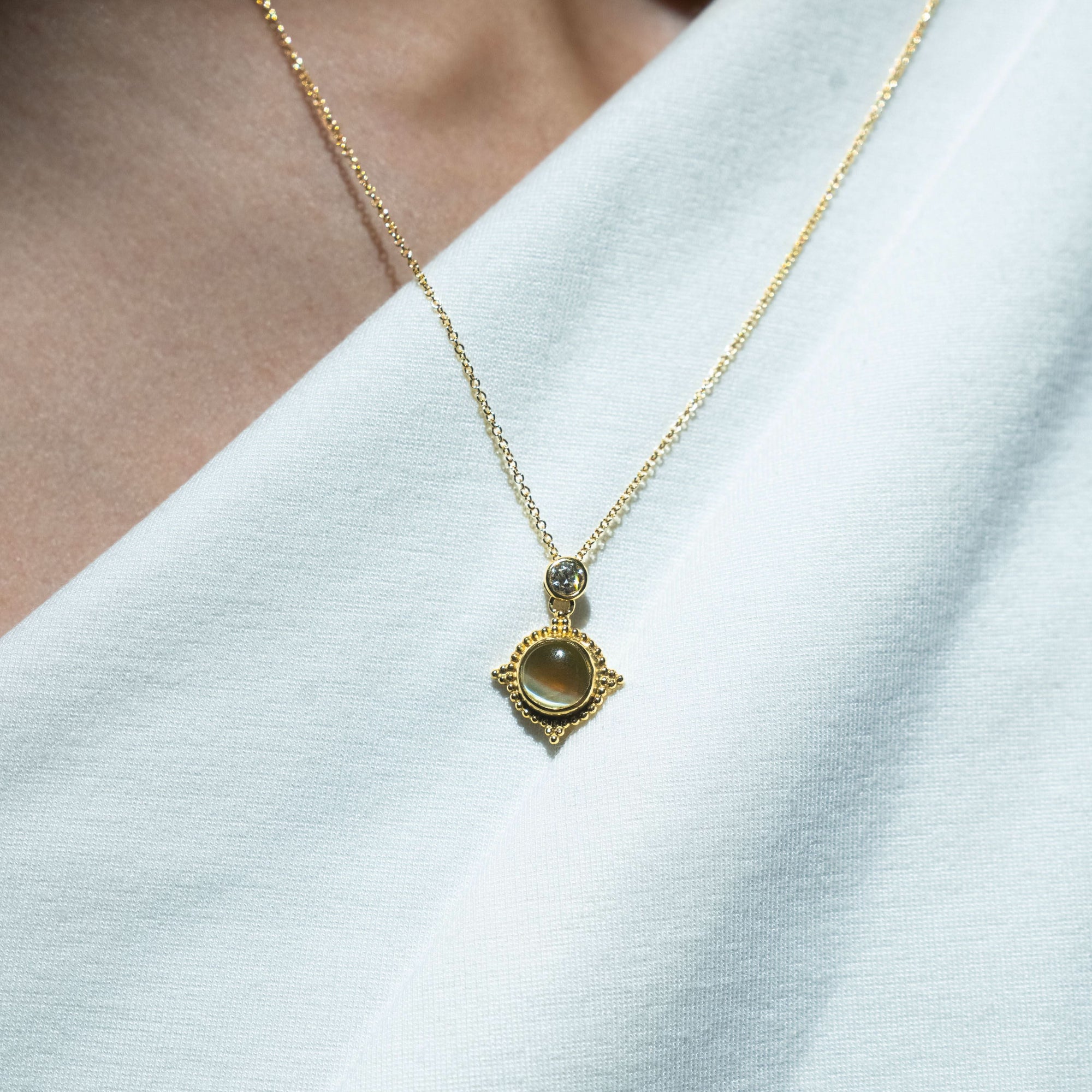 Gold necklace with a diamond and cats eye chrysoberyl pendant on a white background