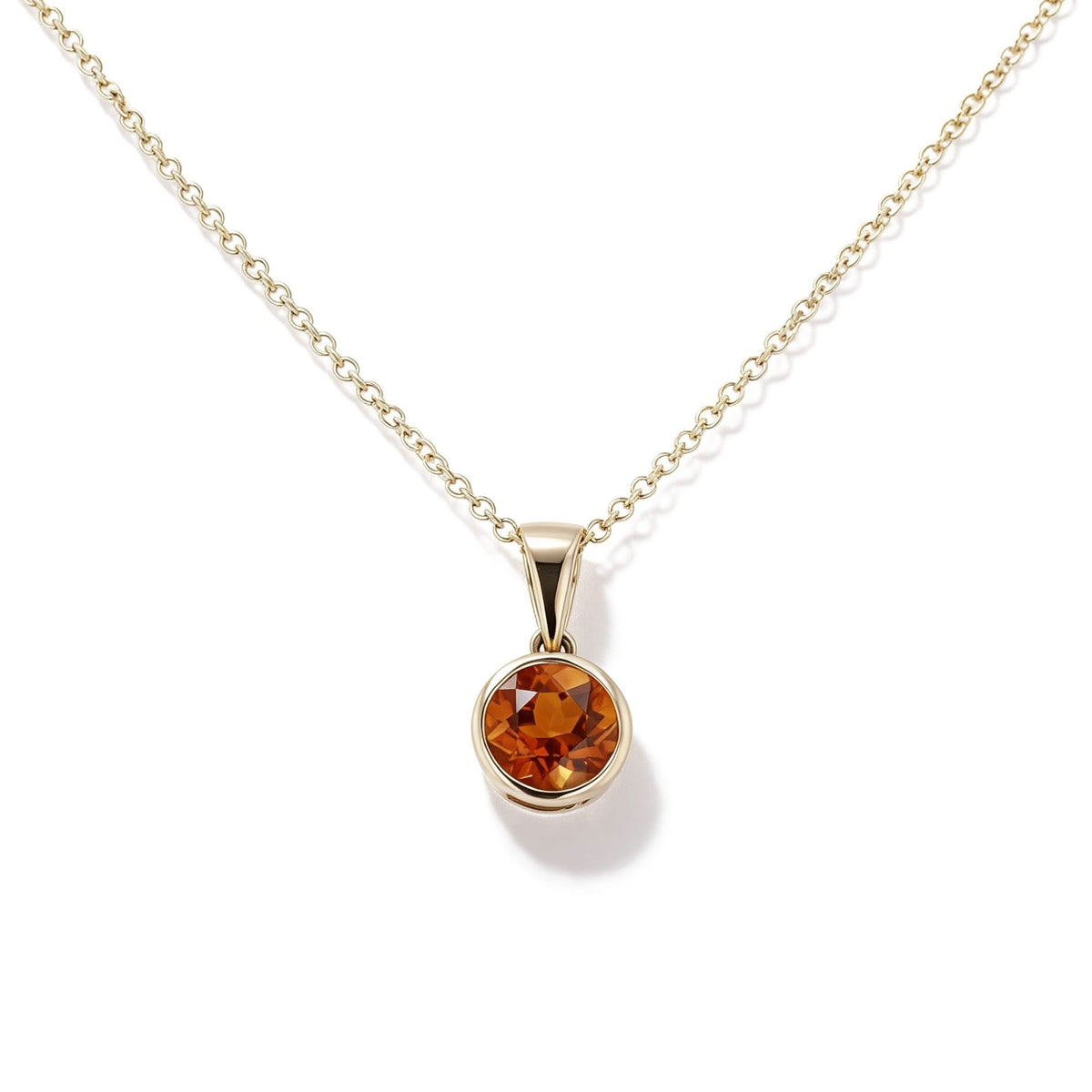A gold chain necklace with a round shaped pendant featuring a faceted citrine gemstone in a gold bezel setting, shown against a plain white background.