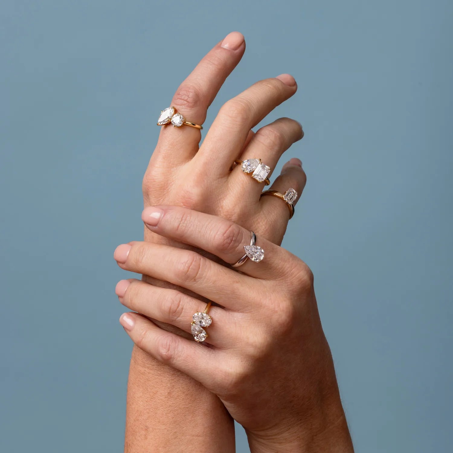 Hand wearing multiple diamond rings on a plain background