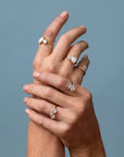 Hand wearing multiple diamond rings on a plain background