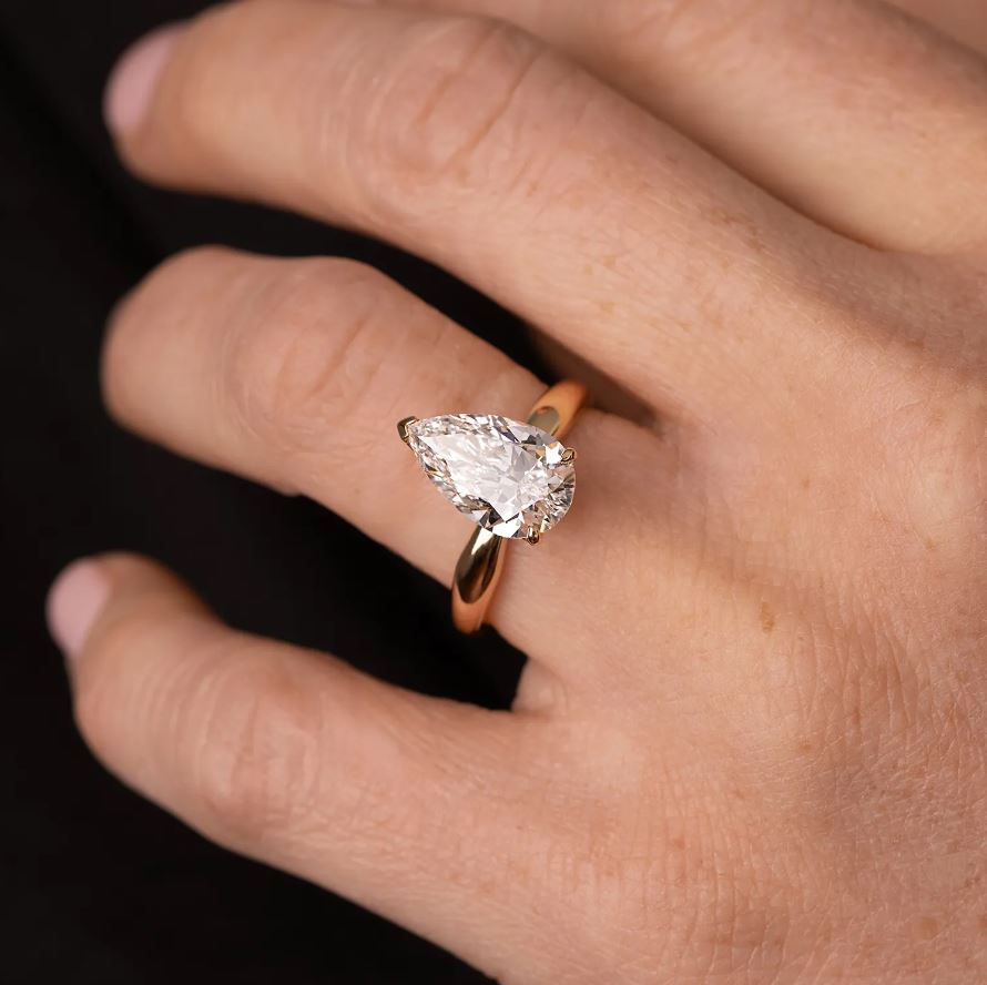 yellow gold ring with a pear-shaped lab grown diamond on a hand against a dark background