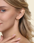 Close-up of a woman wearing a gold hoop earring on a beige background