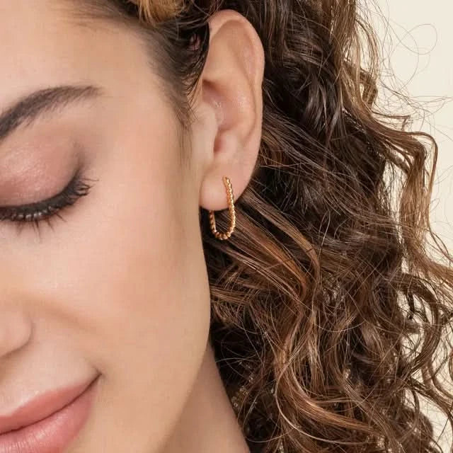 Close-up of a woman wearing a gold hoop earring with a neutral background