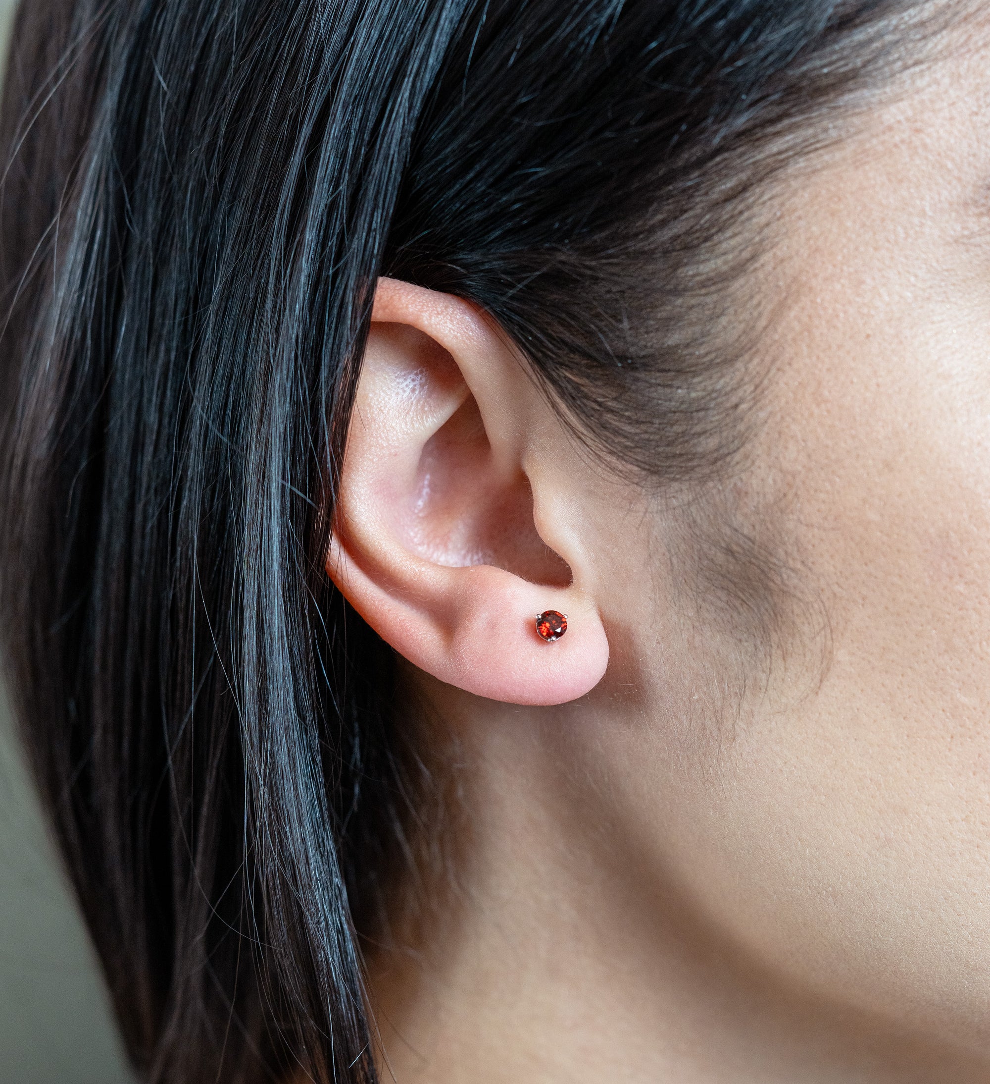 person wearing a white gold and garnet stud in their ear