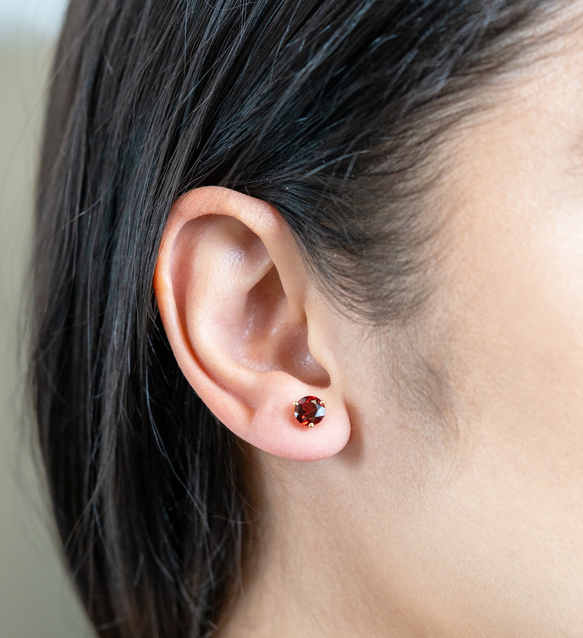 person wearing a yellow gold and garnet stud in their ear