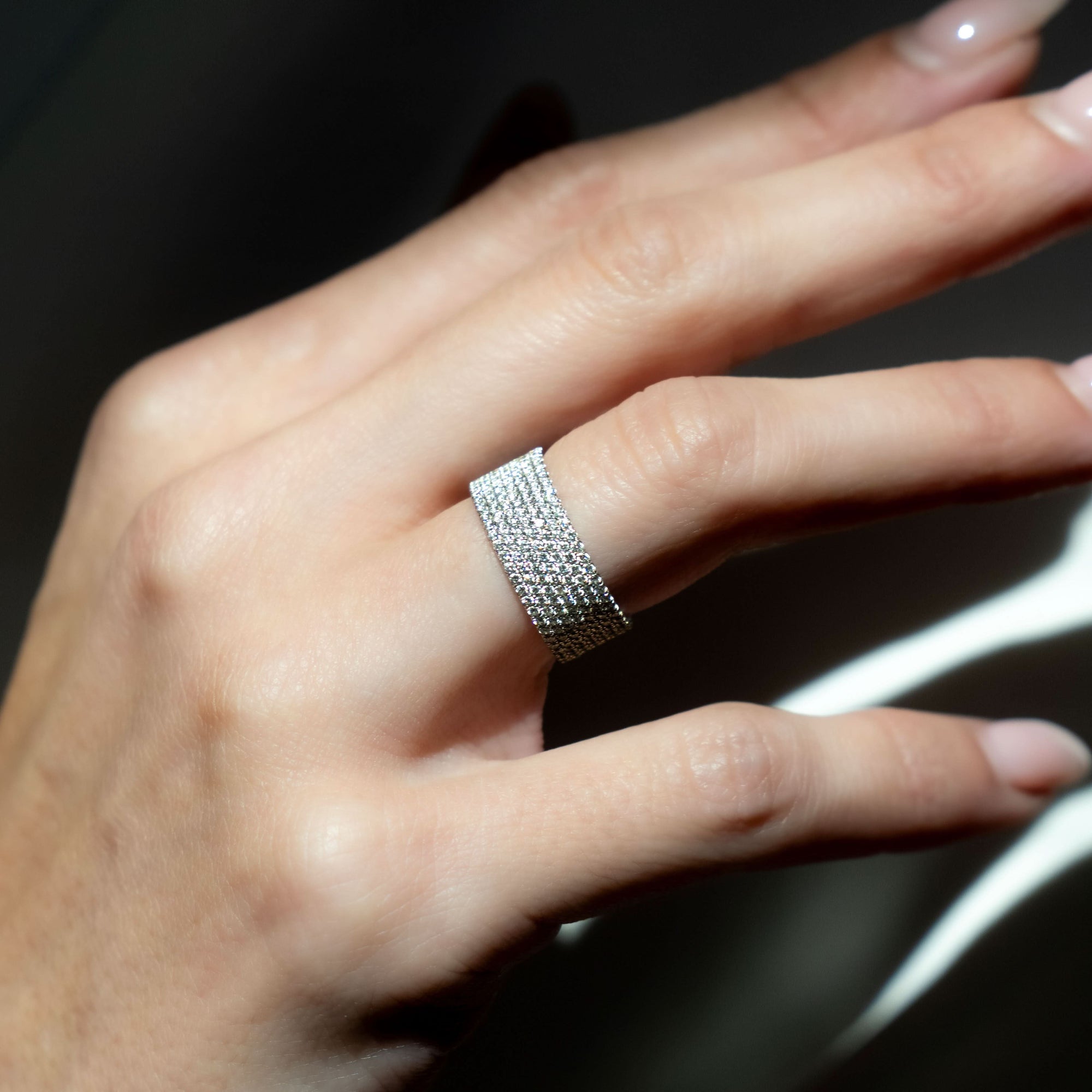 Hand wearing a white gold ring with a pave diamond band against a dark background