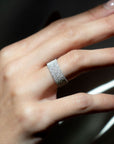 Hand wearing a white gold ring with a pave diamond band against a dark background