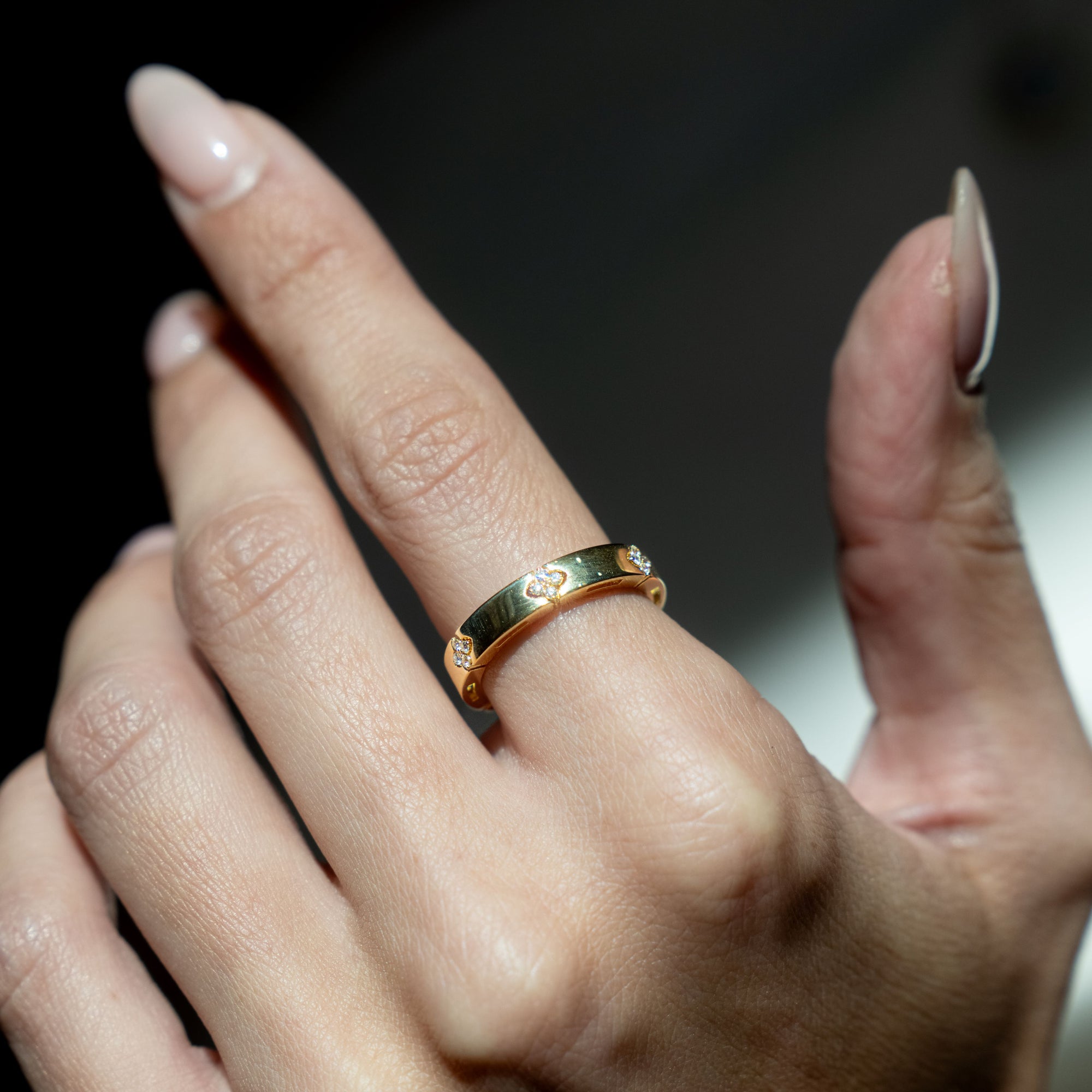 Gold ring with diamonds on a person's finger against a dark background