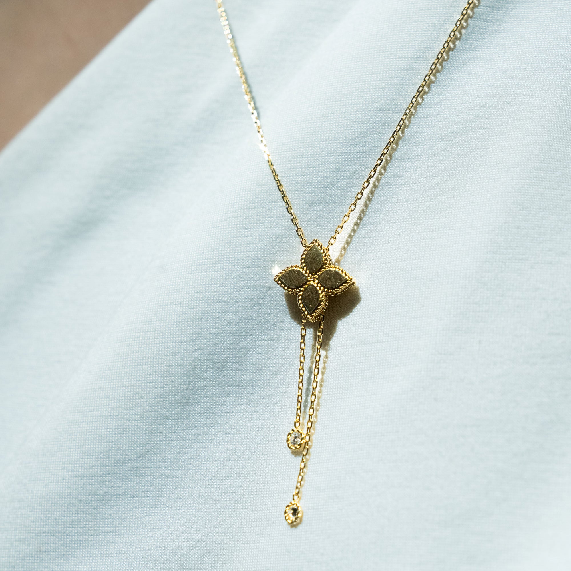 Gold necklace with a floral pendant on a light blue fabric background