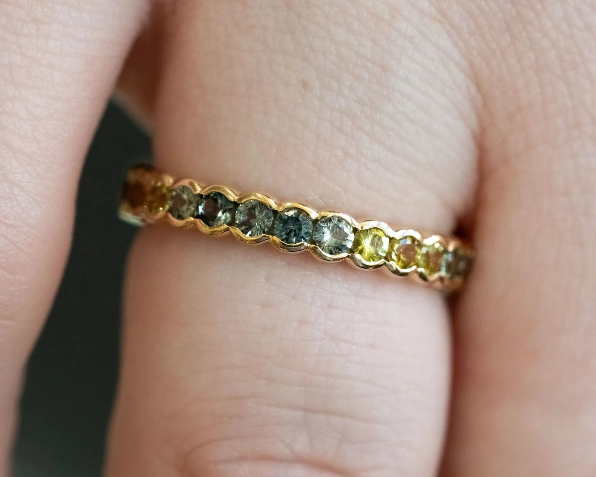 A close-up of a gold  ring with small, multi-colored gemstones set on a person's finger.