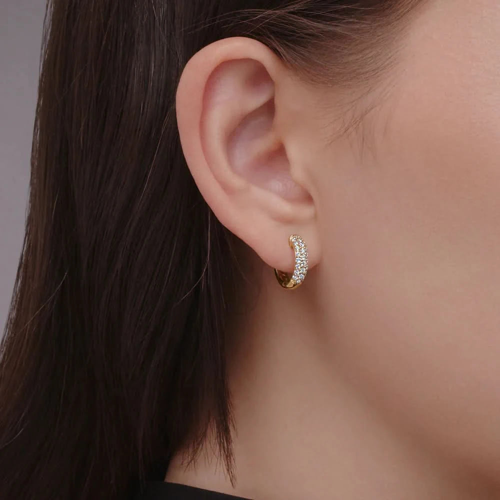 Close-up of an ear wearing a gold and diamond hoop earring against a neutral background