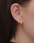 Close-up of an ear wearing a gold and diamond hoop earring against a neutral background
