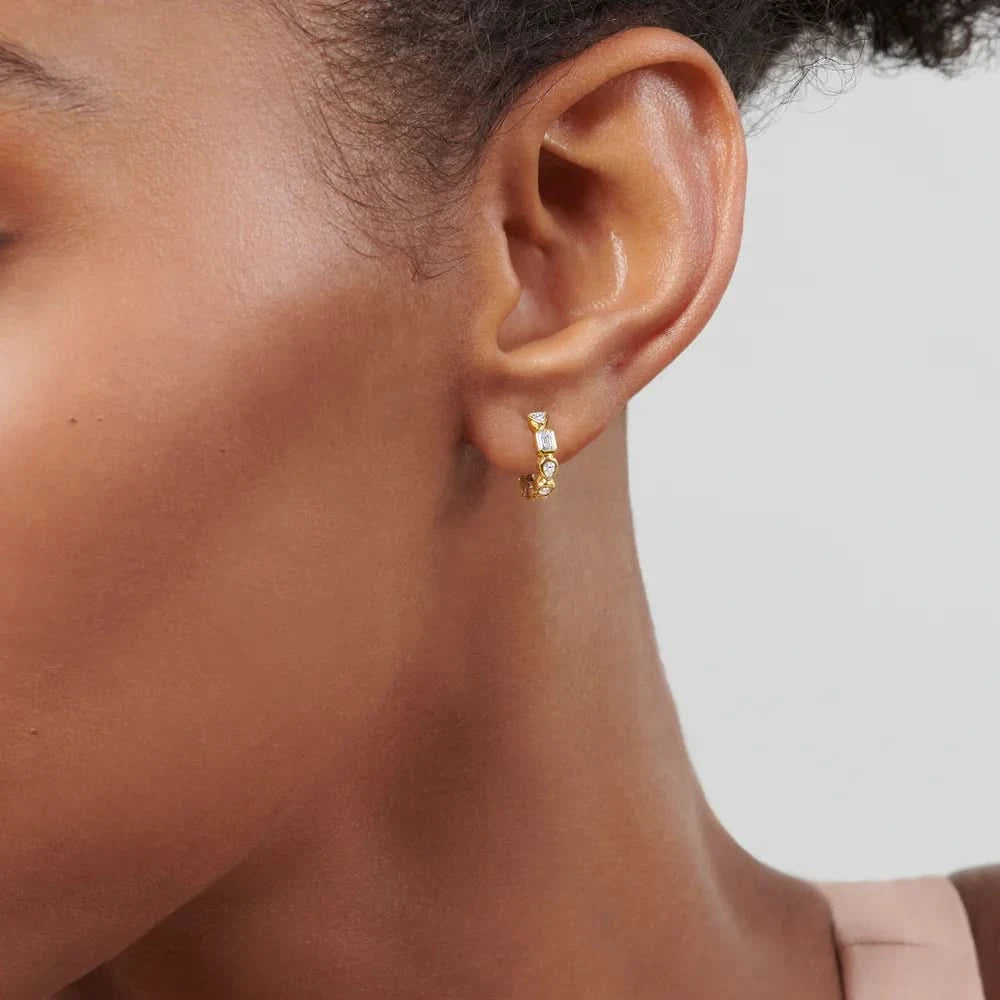 Close-up of an ear wearing a gold hoop earring against a neutral background