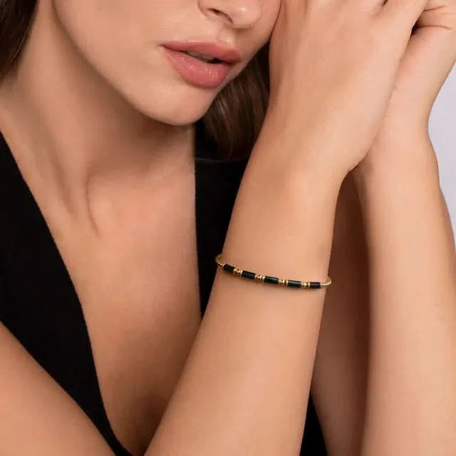Close-up of a woman's arm wearing a gold and black bracelet with a neutral background